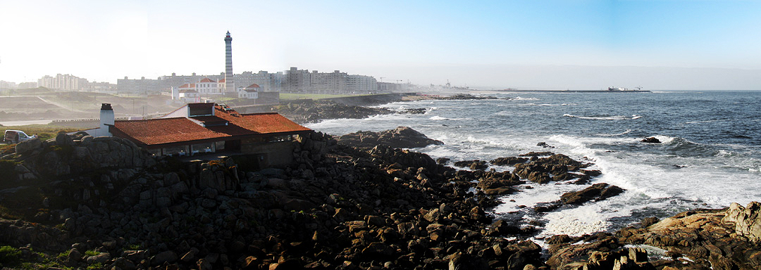 Boa Nova Tea House by Álvaro Siza Vieira on the rocky coastline of Leça da Palmeira, Portugal, with the lighthouse in the background.