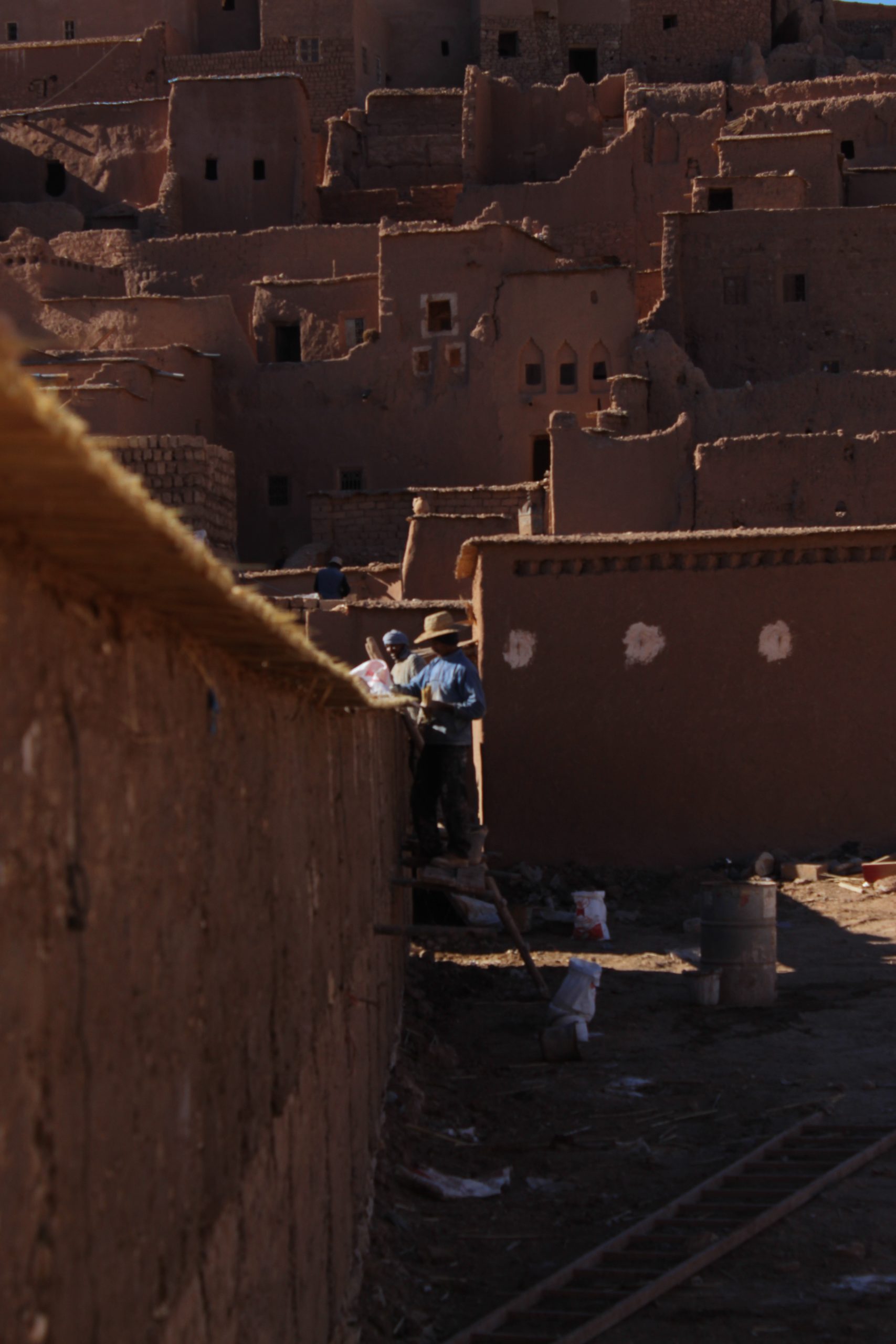 Local workers repairing an earthen wall in Aït Ben Haddou using traditional techniques.