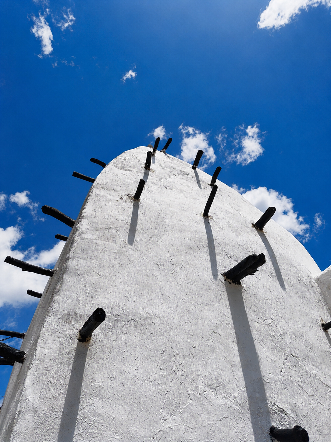 Upward view of the Larabanga Mosque in northern Ghana, showing earthen walls reinforced with projecting timber beams against a deep blue sky.